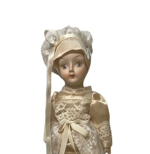 PORCELAIN DOLL 14" WEARING CREAM LACE SATIN GOWN W/MATCHING LACE BONNET.