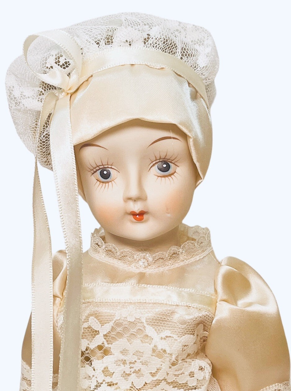 PORCELAIN DOLL 14" WEARING CREAM LACE SATIN GOWN W/MATCHING LACE BONNET.